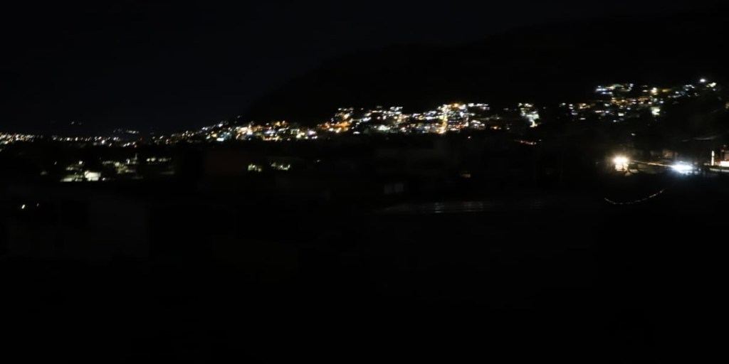 Vista nocturna de una ciudad iluminada, con luces en las colinas y edificios visibles.