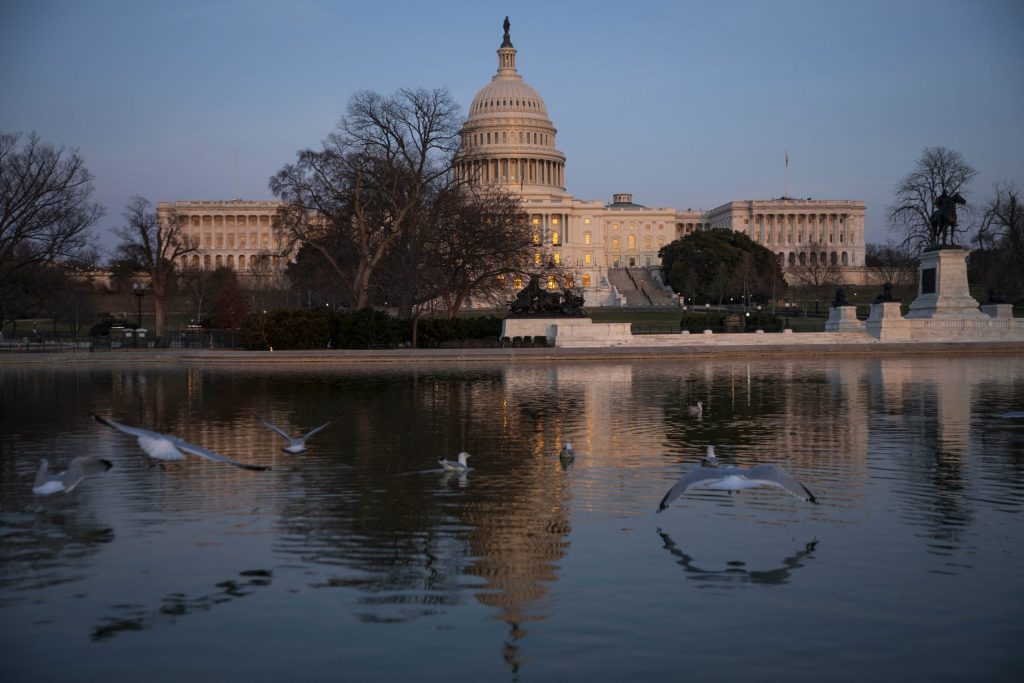 Vista del Capitolio de los Estados Unidos al atardecer, con aves volando sobre el agua en primer plano.