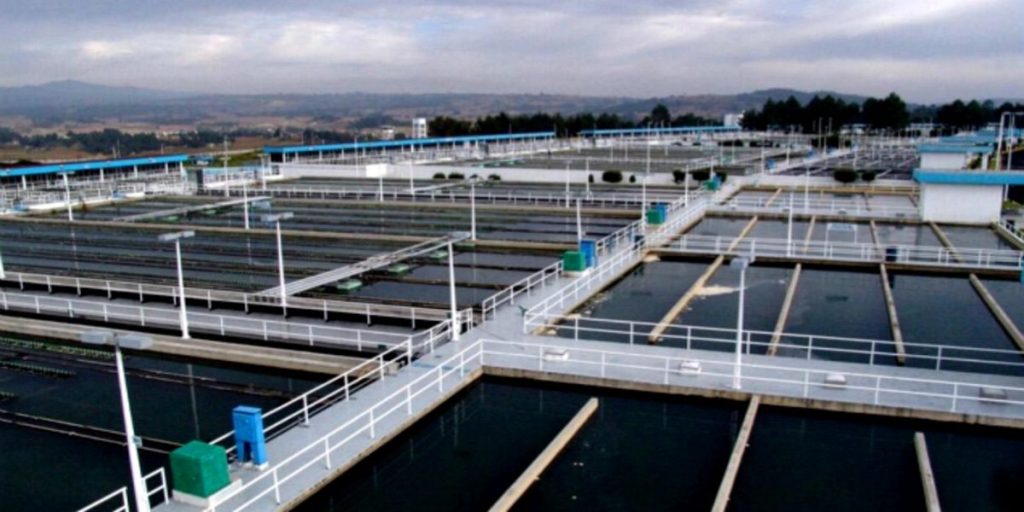 Aerial view of a large water treatment facility featuring multiple interconnected pools and walkways under a cloudy sky.