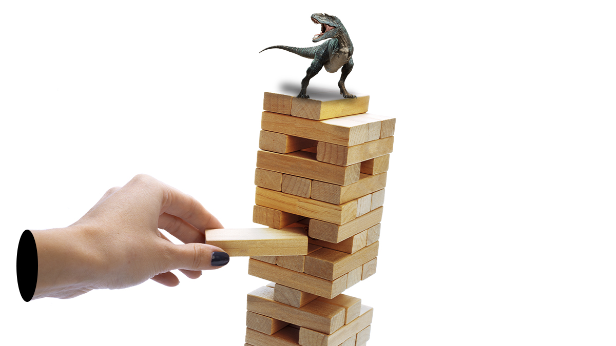 Una mano tirando un juego de jenga con un dinosaurio arriba
