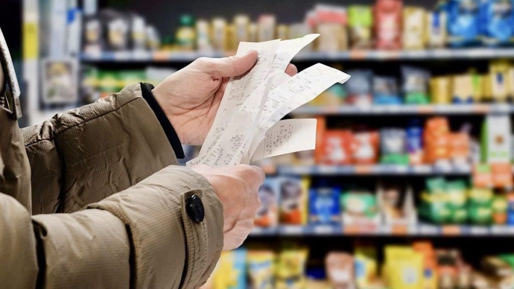 Persona sosteniendo varios recibos de compras frente a estanterías de supermercado.