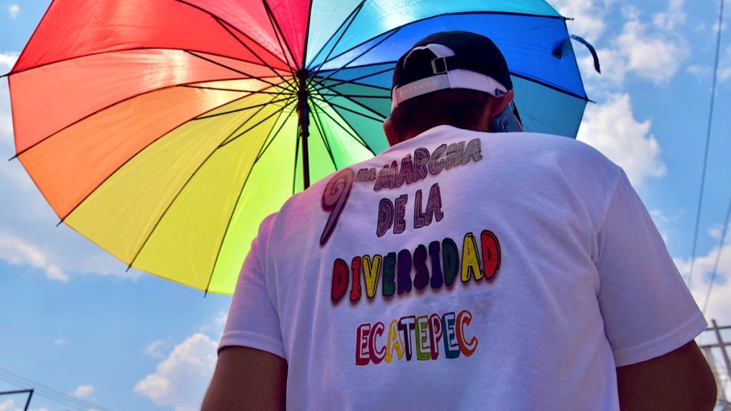 Persona de espaldas con camiseta que dice 'Marcha de la Diversidad Ecatepec' bajo un paraguas colorido, en un contexto de celebración de diversidad.