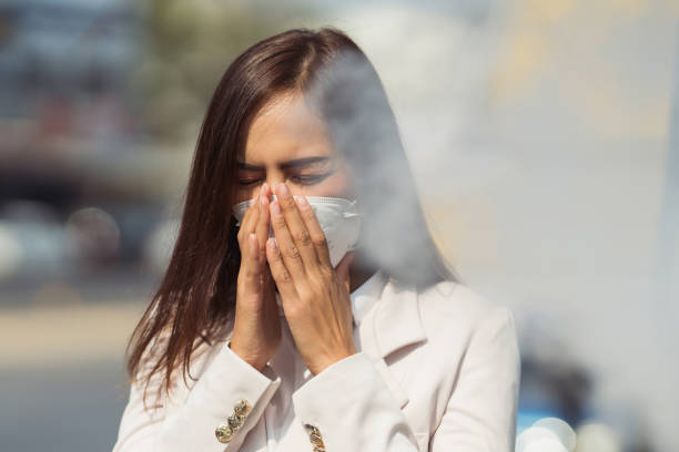 Mujer con mascarilla frotándose la cara, visiblemente afectada por la contaminación del aire.