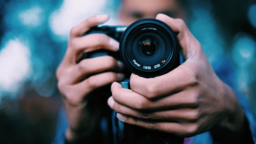 Persona sosteniendo una cámara con lentes de cerca, fondo desenfocado con luces suaves.