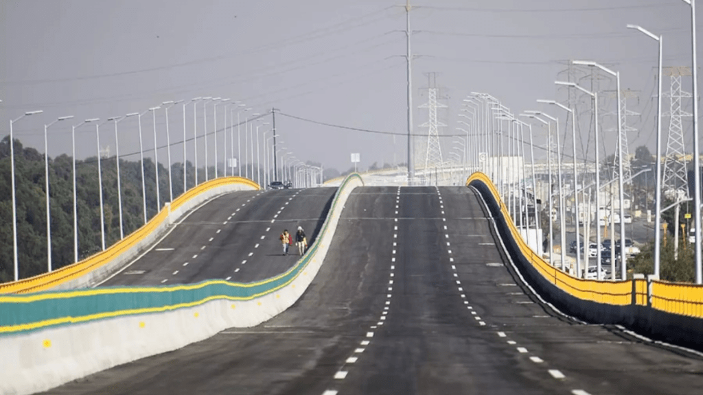Vista de una carretera amplia y vacía con una pintura de líneas de tráfico, bordeada por barandas amarillas y verdes, y con dos ciclistas en el centro.