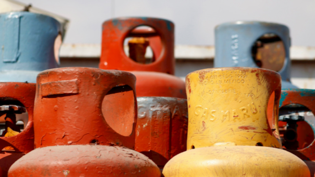 Tambores de gas LP de varios colores apilados, visibles en un entorno exterior.