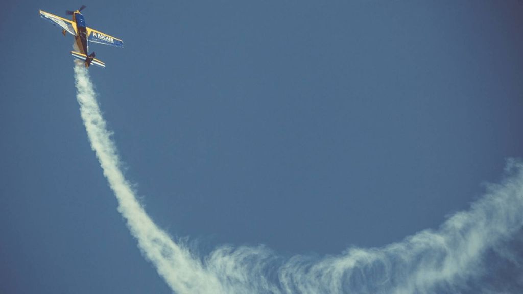 An acrobatic airplane performing a loop, leaving a trail of white smoke against a blue sky.