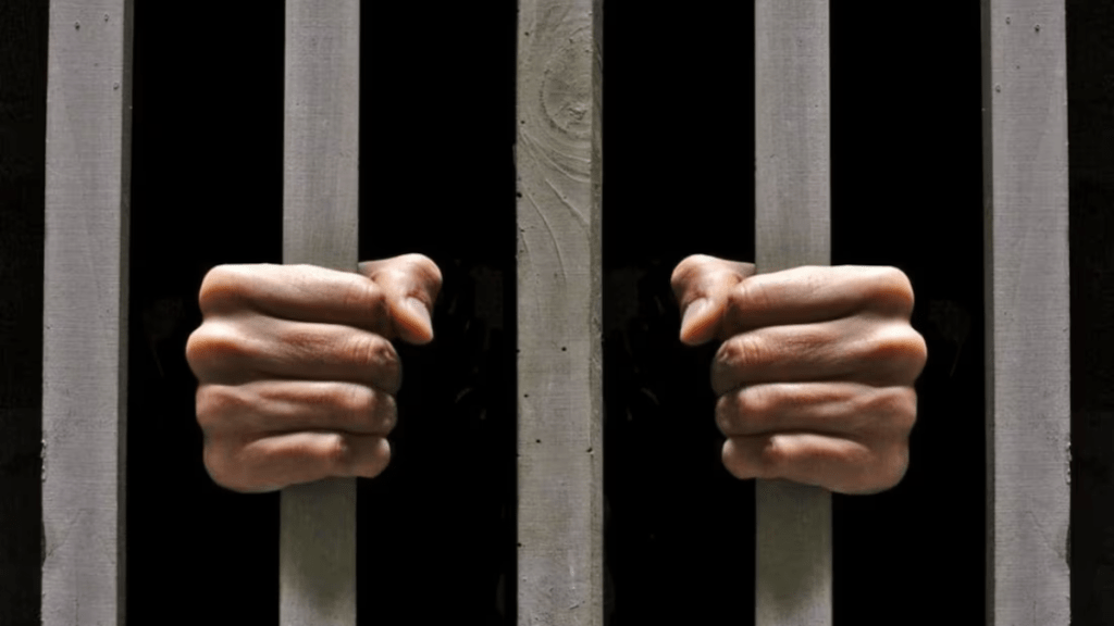 Manos aferrándose a las rejas de una celda.