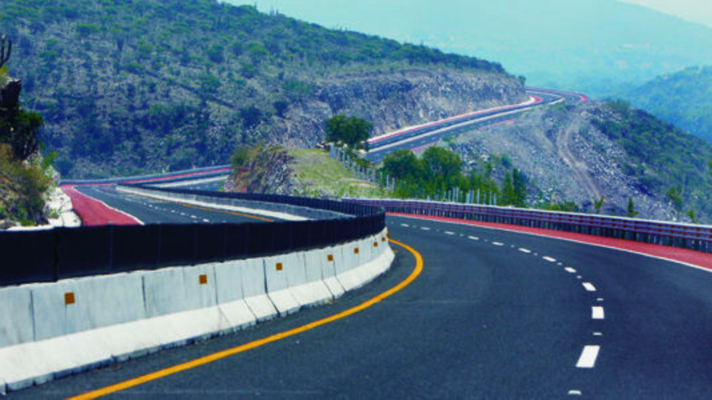 A winding road with a picturesque mountainous landscape in the background, featuring green vegetation on the hillsides.