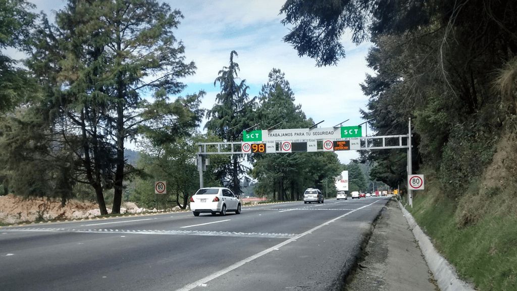 A busy road with traffic signs displaying speed limits and safety information, surrounded by trees and a clear sky.