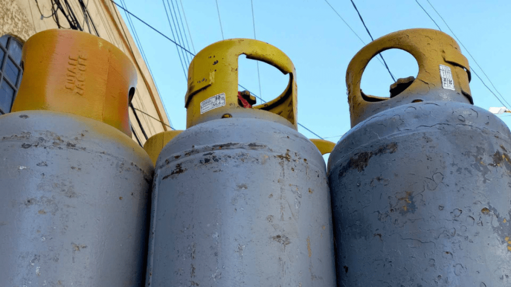 Tres tanques de gas LP apilados, con tapas amarillas y cuerpos metálicos grises, contra un fondo de cables y cielo despejado.
