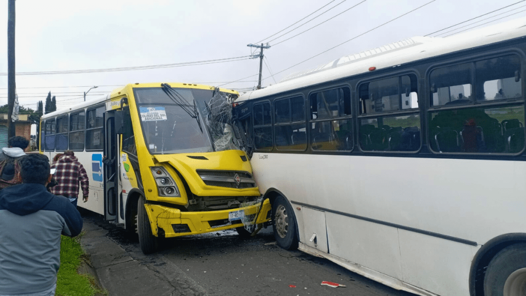 Accidente de tránsito entre un autobús amarillo y un autobús blanco en Toluca, con varios espectadores en la escena.