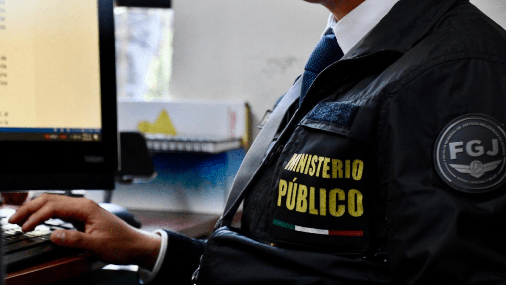 Un funcionario del Ministerio Público trabajando en una computadora, con un enfoque en su chaqueta y un monitor con texto en el fondo.