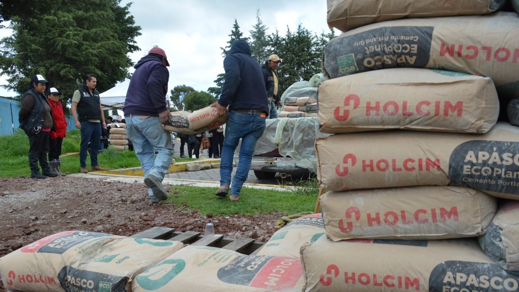 Un grupo de personas en un sitio de construcción, cargando sacos de cemento Holcim mientras otros observan.