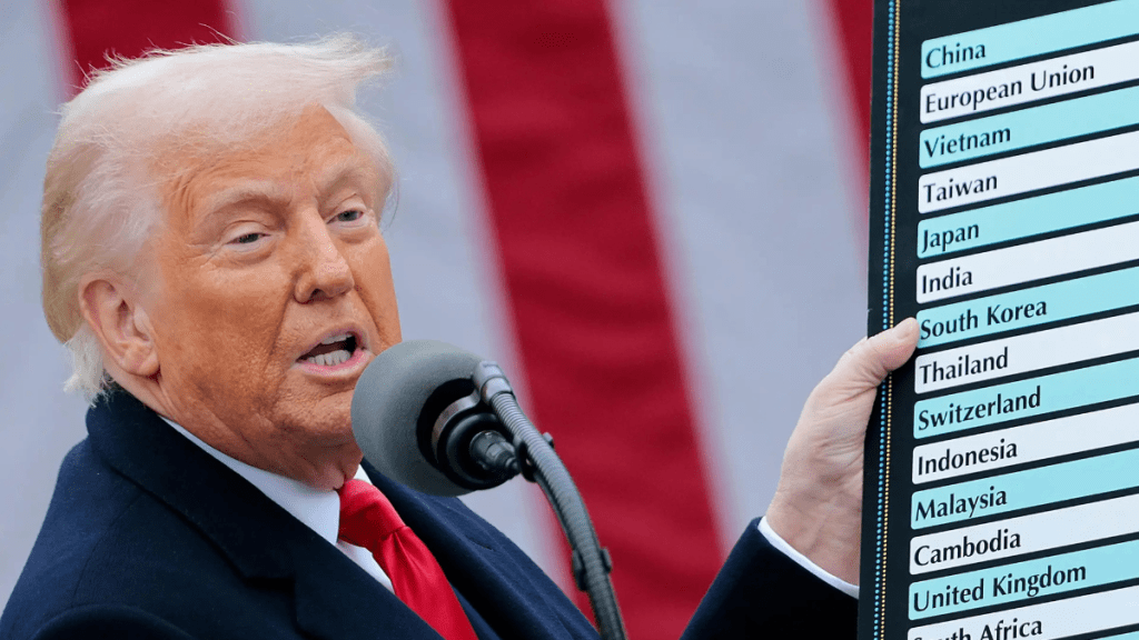 Donald Trump hablando en un micrófono y sosteniendo un cartel con nombres de países en una conferencia de prensa.