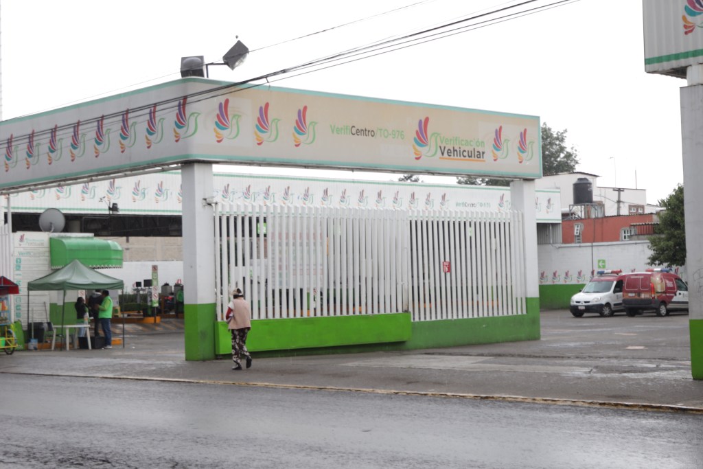 Entrada de un verificentro vehicular en el Estado de México, con señalización y diseño colorido. Se observan personas y vehículos en las inmediaciones.