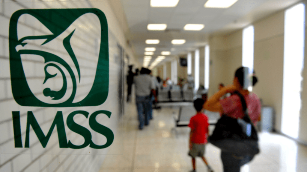 Logotipo del IMSS en primer plano con personas caminando en un pasillo amplio y luminoso.