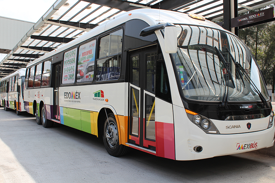 Autobús del sistema Mexibús, colorido y moderno, estacionado en una terminal bajo techo, con publicidad visible en sus ventanas.