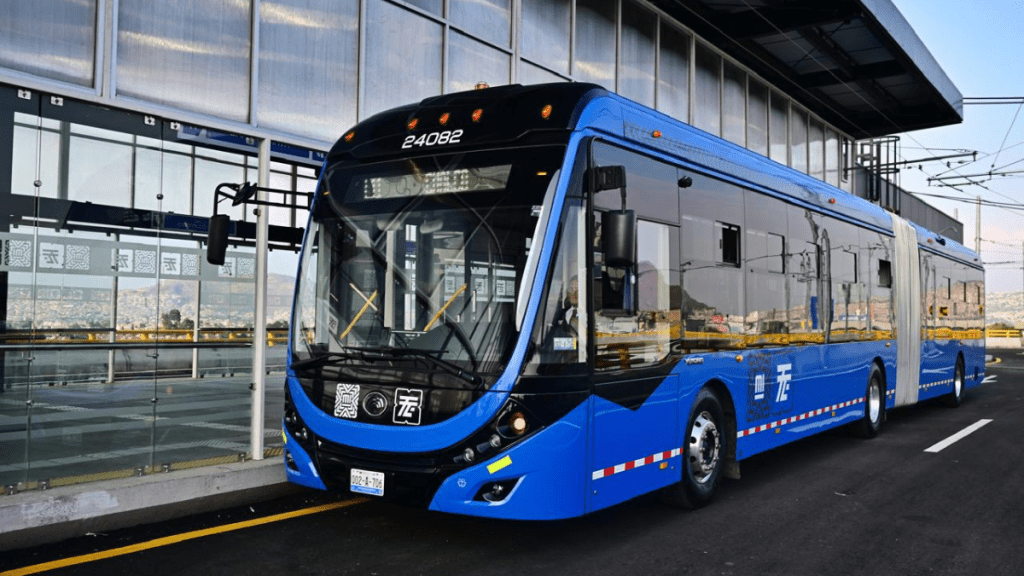 Autobús Mexibús de color azul en una terminal, con un diseño moderno y estaciones cercanas visibles en el fondo.