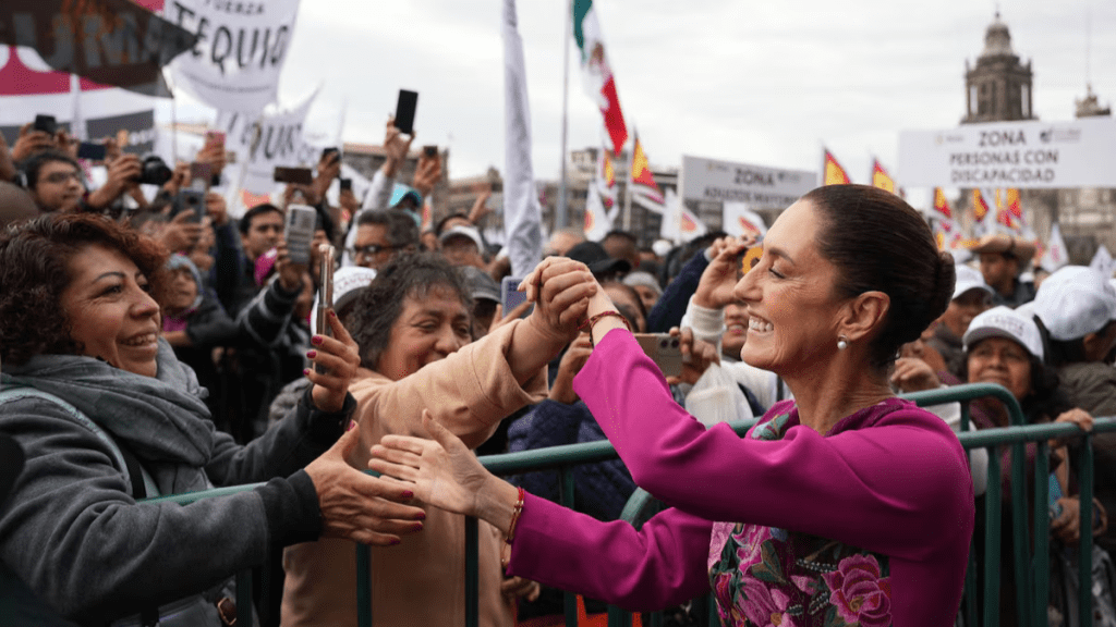 Claudia Sheinbaum, presidenta de México, interactúa con simpatizantes durante un evento público, rodeada de multitudes y pancartas.