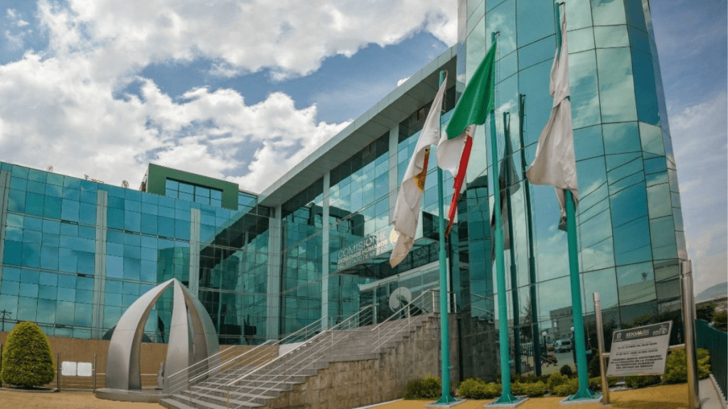 Fachada moderna de un edificio de oficinas de cristal, con banderas ondeando en frente y un jardín bien cuidado.