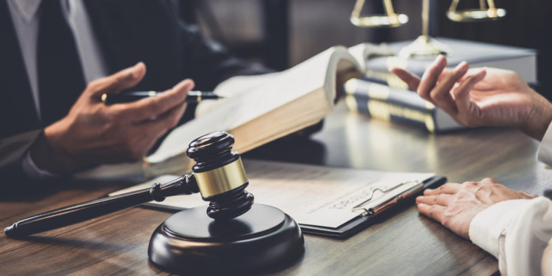 Un juez gavila en el escritorio junto a manos de abogados discutiendo sobre documentos legales y un libro de leyes.