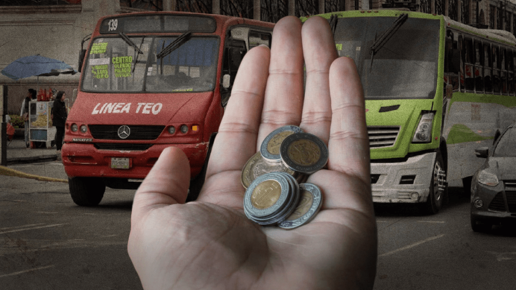 Una mano sosteniendo monedas frente a dos autobuses color rojo y verde en una calle de la ciudad.