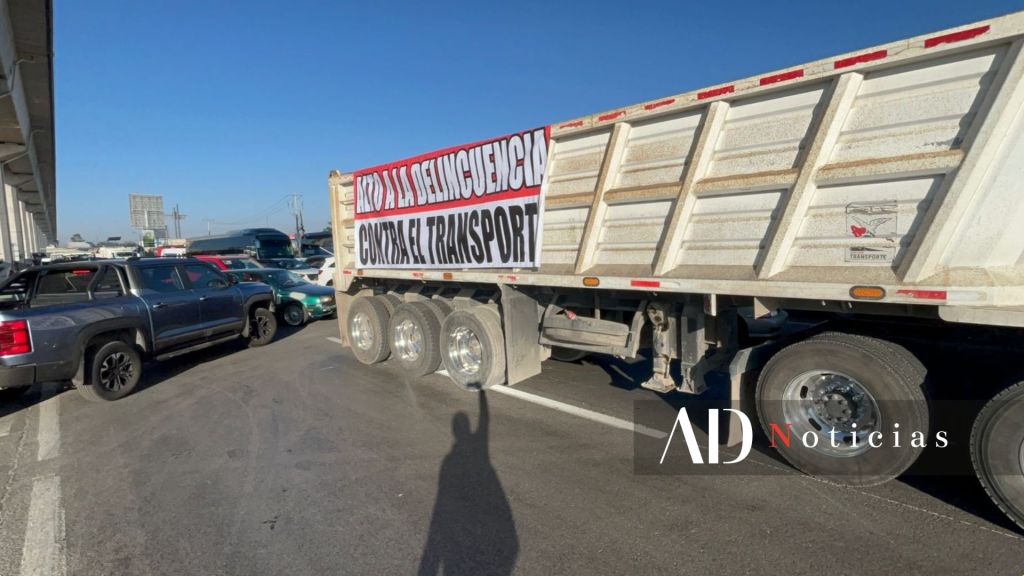 Camión de carga bloqueando un carril de la carretera con un cartel que dice 'Alto a la delincuencia contra el transporte'.