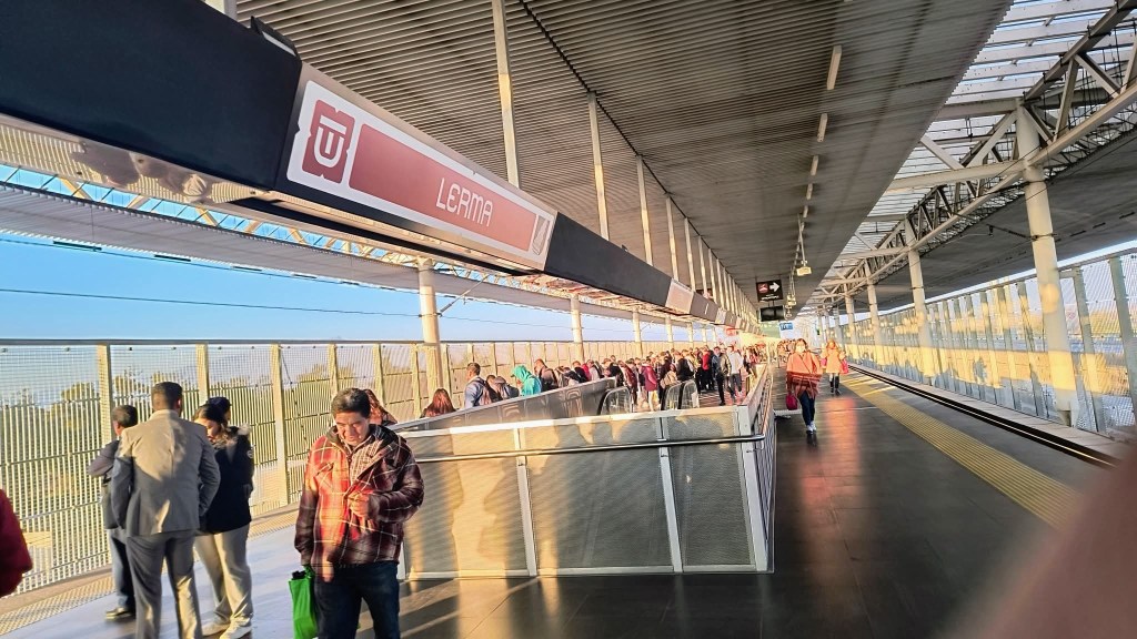 Estación del Tren Interurbano El Insurgente en Lerma, con una multitud de pasajeros esperando en el andén, iluminada por la luz del sol de la mañana.