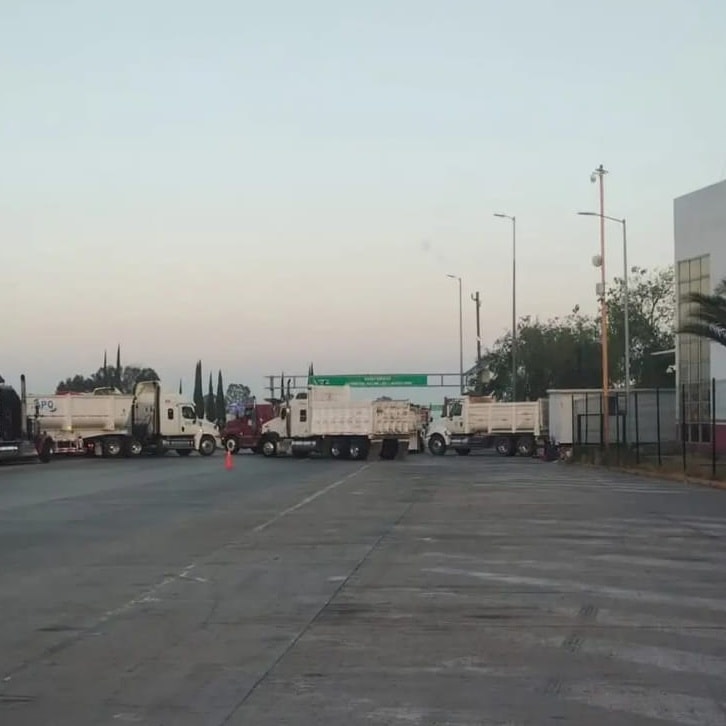 Camiones de transporte bloqueando una carretera en México, impidiendo el paso vehicular y generando congestión.