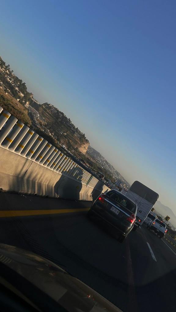 Tráfico congestionado en la autopista, con vehículos y un camión detenidos, junto a un paisaje montañoso de fondo.