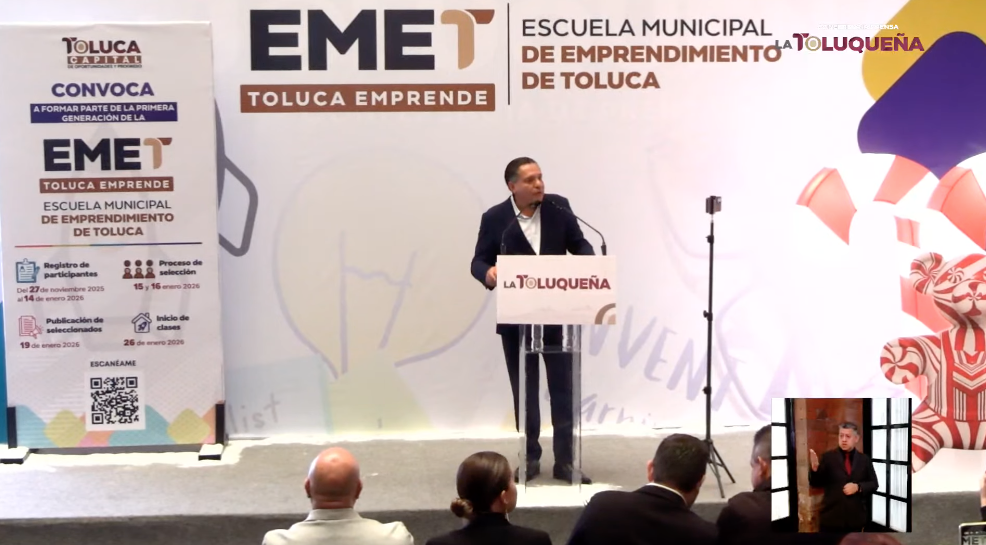 Presentación de la convocatoria para la Escuela Municipal de Emprendimiento de Toluca, con un orador de pie frente a un podio y un fondo que destaca el logo de la escuela y la información sobre el programa.