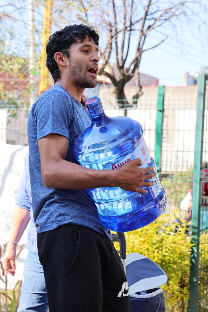 Hombre joven sosteniendo un garrafón de agua del programa Agua Bienestar, en un entorno urbano.