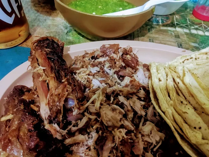Plato de carnitas acompañadas de tortillas y salsa verde, sobre una mesa decorada.
