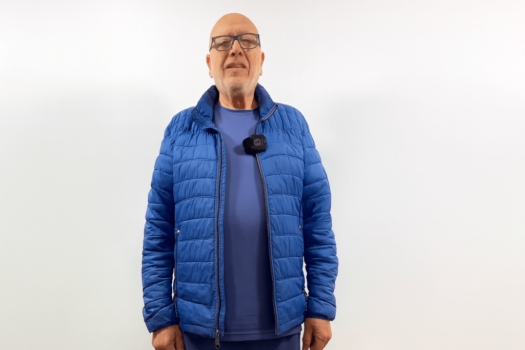 Hombre de pie, vistiendo una chaqueta azul y una camiseta azul, con gafas y cabello corto, posando frente a un fondo blanco.