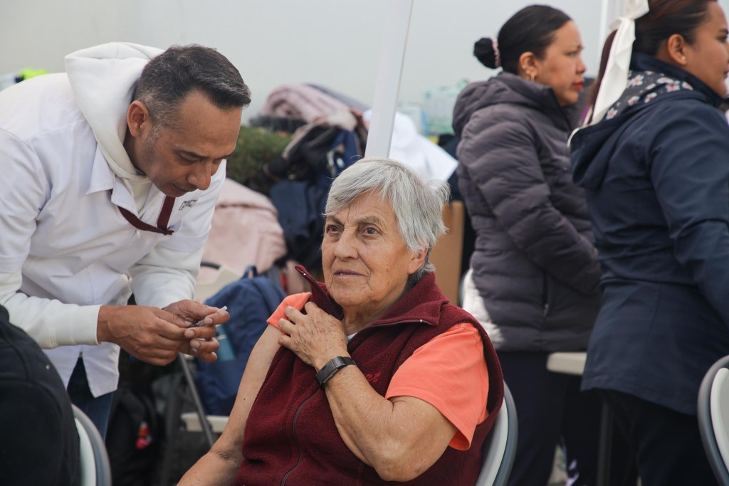 Un profesional de la salud administrando una vacuna a una mujer mayor en un evento de vacunación.