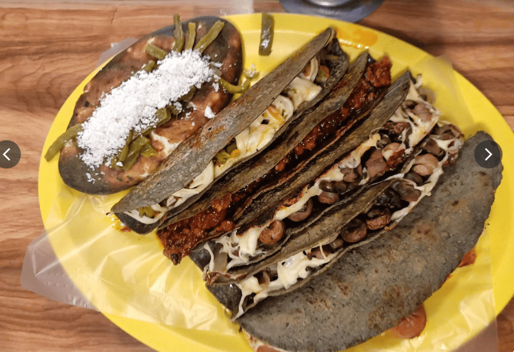 Un plato colorido con varias quesadillas de maíz negro y un pambazo, acompañado de frijoles y espárragos.
