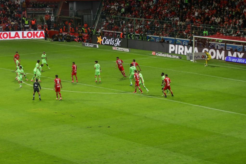Jugadores del equipo Toluca en acción durante un partido contra el equipo Bravos de Juárez en el estadio, con la afición animando al fondo.