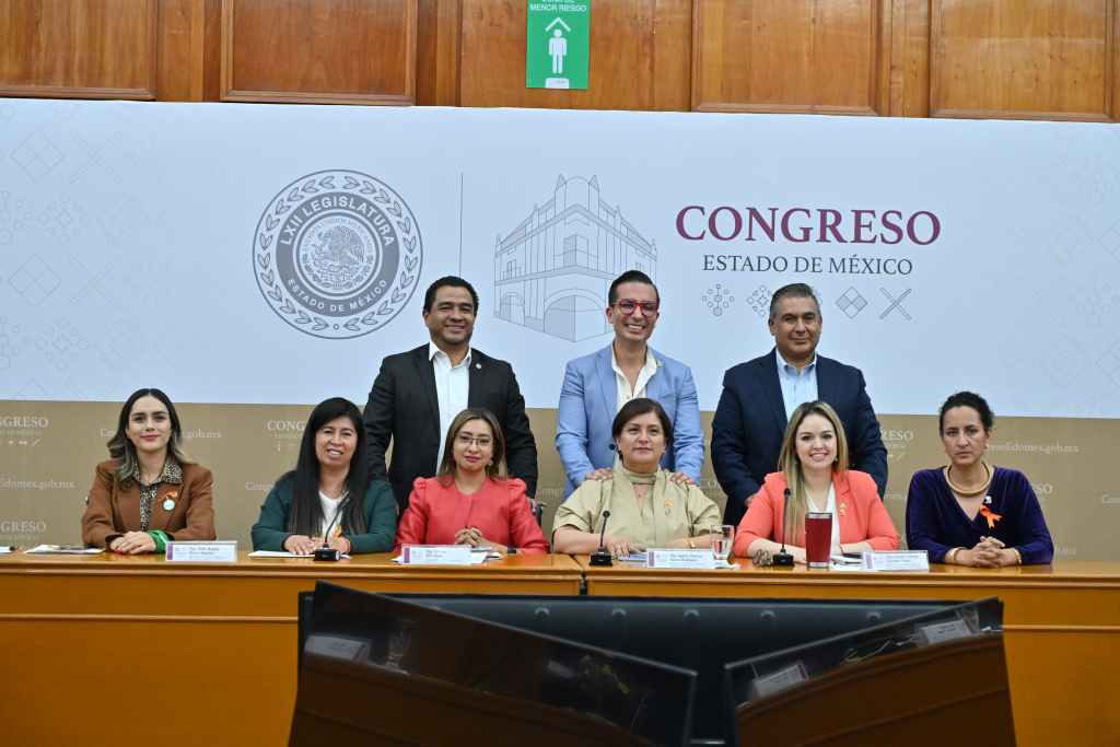 Grupo de legisladores en el Congreso del Estado de México, posando frente a una mesa con documentos, en un ambiente institucional.