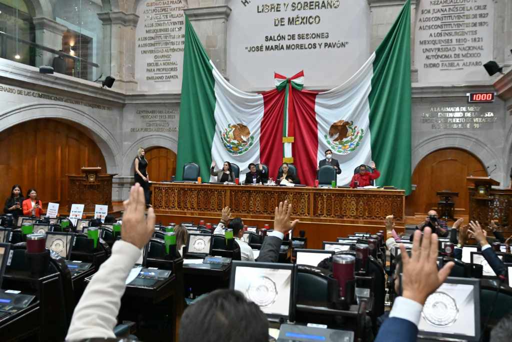 Sesión en el Congreso del Estado de México con diputados levantando la mano, rodeados por las banderas de México.