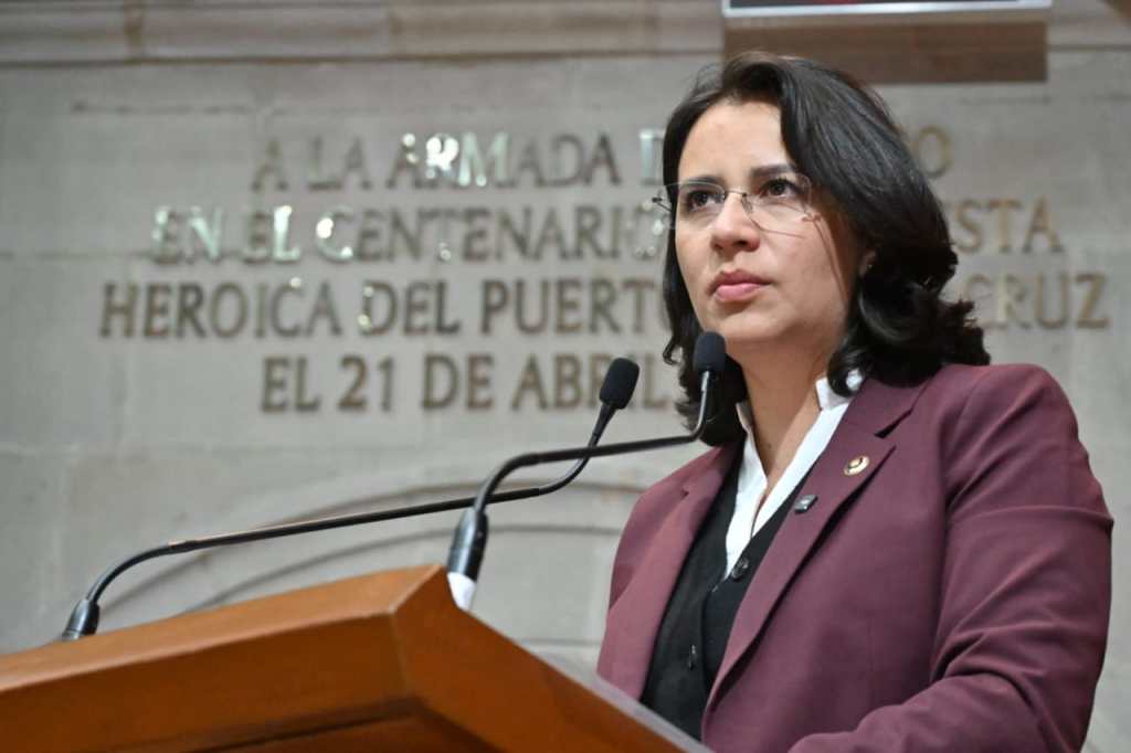 Una diputada habla desde el podio en el Congreso mexiquense, con una placa conmemorativa al fondo.