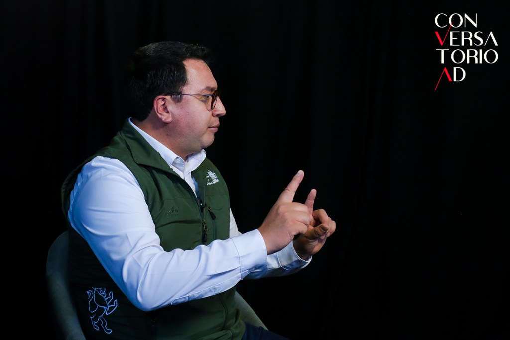 Entrevista con el alcalde de Lerma, Miguel Ángel Ramírez Ponce, en un fondo oscuro, mientras gesticula con las manos durante la conversación.