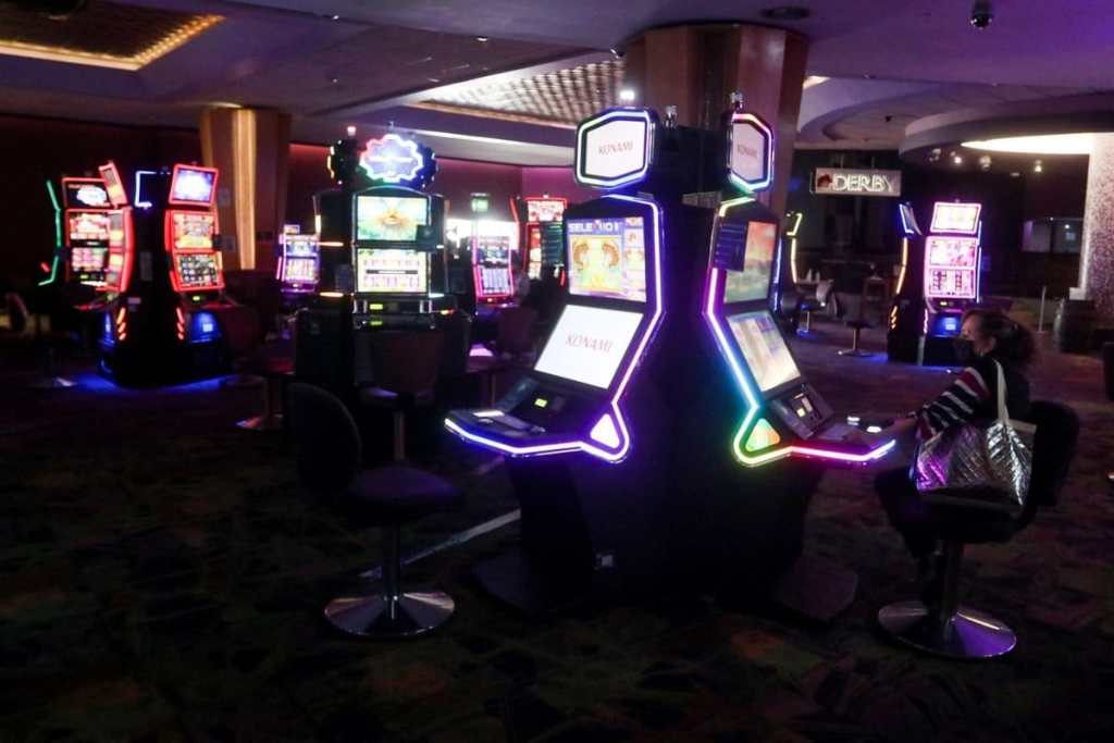 Interior de un casino con varias máquinas tragamonedas iluminadas y una persona jugando en una máquina.