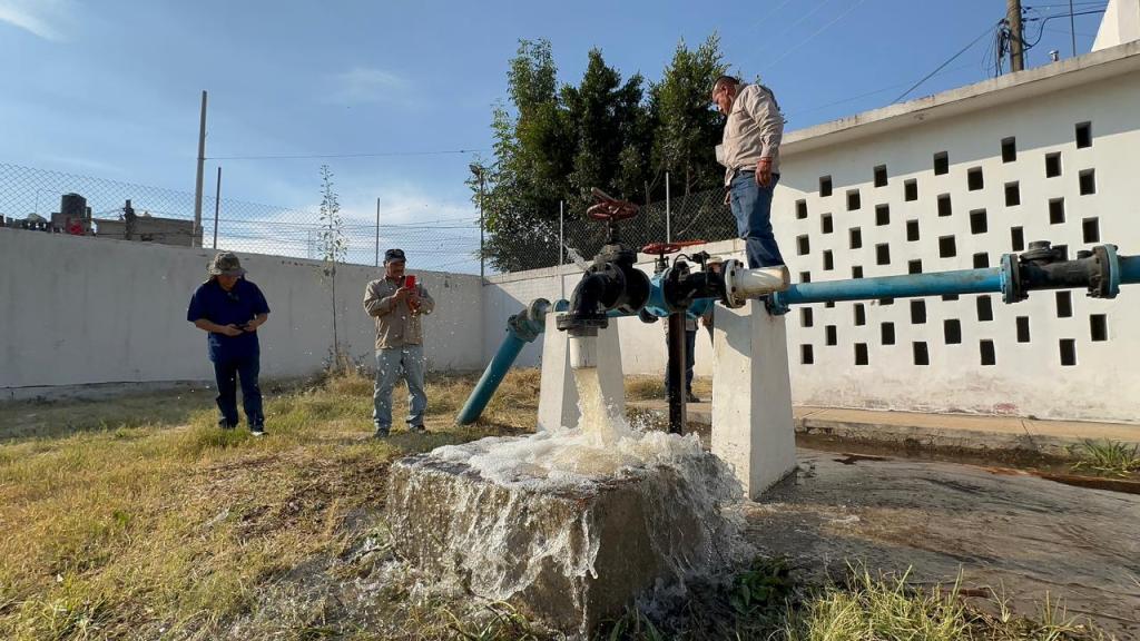 Tres trabajadores supervisan el funcionamiento de un pozo de agua potable en la colonia Luis Echeverría, mientras el agua fluye desde la tubería hacia el suelo.