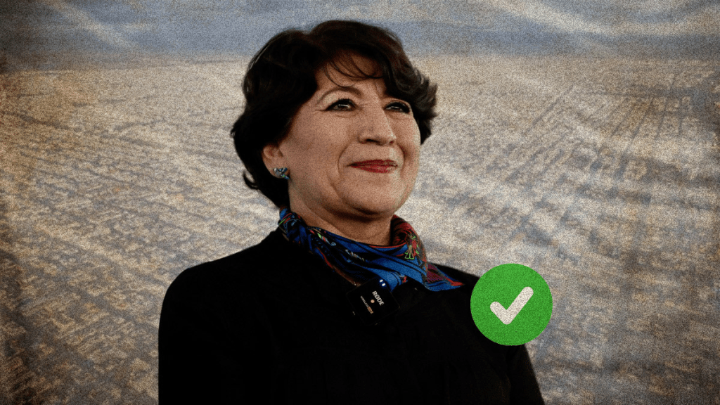 Retrato de una mujer sonriendo, con una blusa negra y una bufanda colorida en el cuello, en un entorno natural con campos al fondo. Se incluye un ícono verde de 'check' en la esquina inferior derecha.