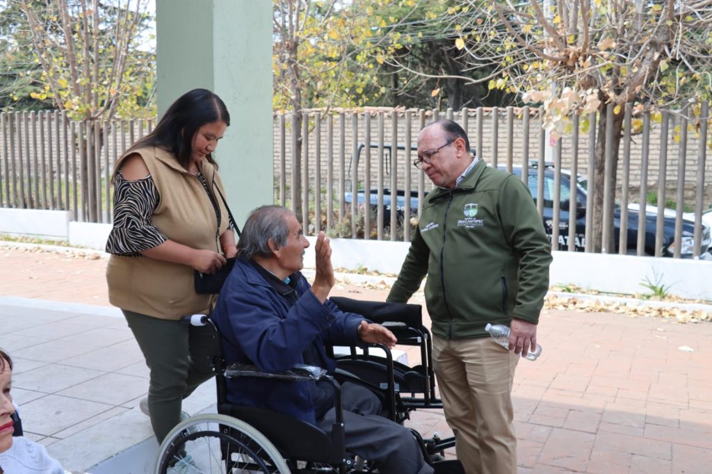 Un alcalde y una mujer conversan con un adulto mayor en silla de ruedas durante la entrega de aparatos funcionales, en un evento por el Día Internacional de las Personas con Discapacidad.