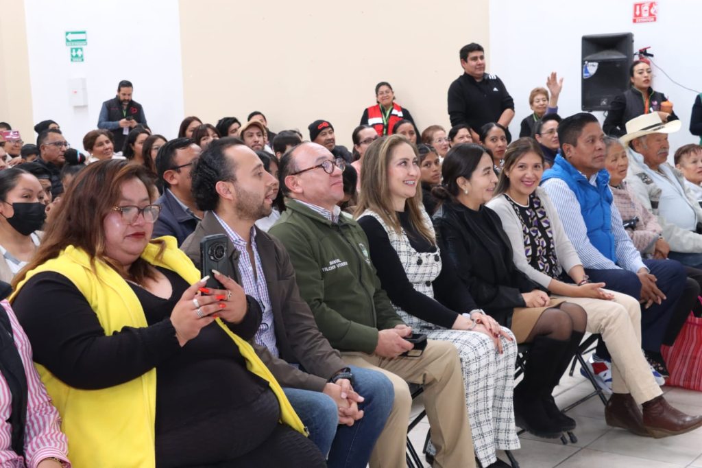 Grupo de personas sentadas en un evento, prestando atención y sonriendo, durante la entrega de aparatos funcionales en el marco del Día Internacional de las Personas con Discapacidad.