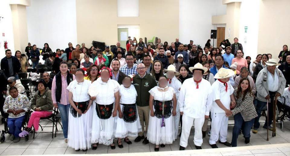 Una multitud de personas reunidas en un evento comunitario, con varios habitantes, incluyendo a personas con discapacidad, en una sala amplia.