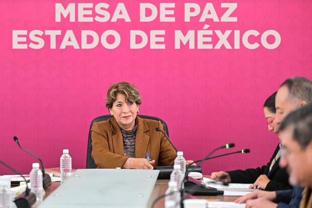 Reunión de la Mesa de Paz del Estado de México, con un enfoque en la prevención de extorsiones, donde se observa a una mujer en primer plano junto a otros funcionarios.