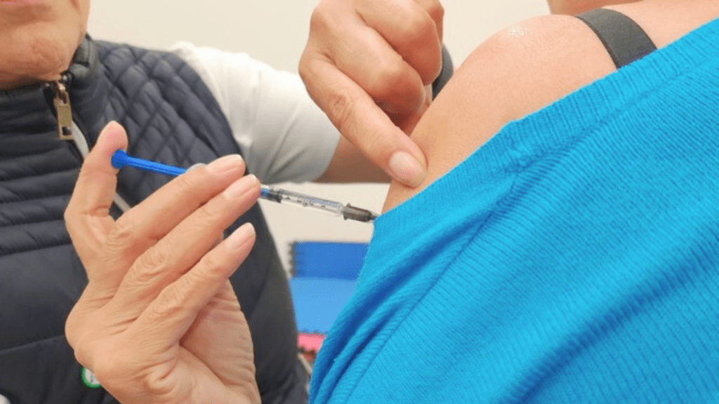A healthcare professional administering a vaccine via injection into the shoulder of a person wearing a blue shirt.